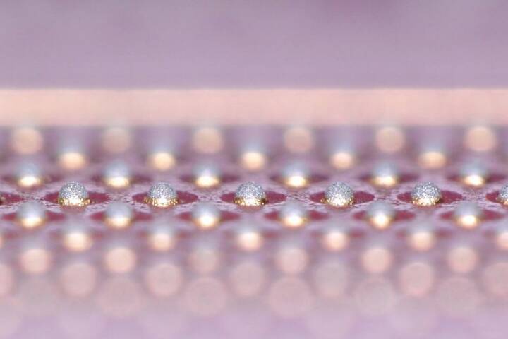 Enlarged side view of multiple solder paste dots arranged in parallel rows of uniform size on a surface.